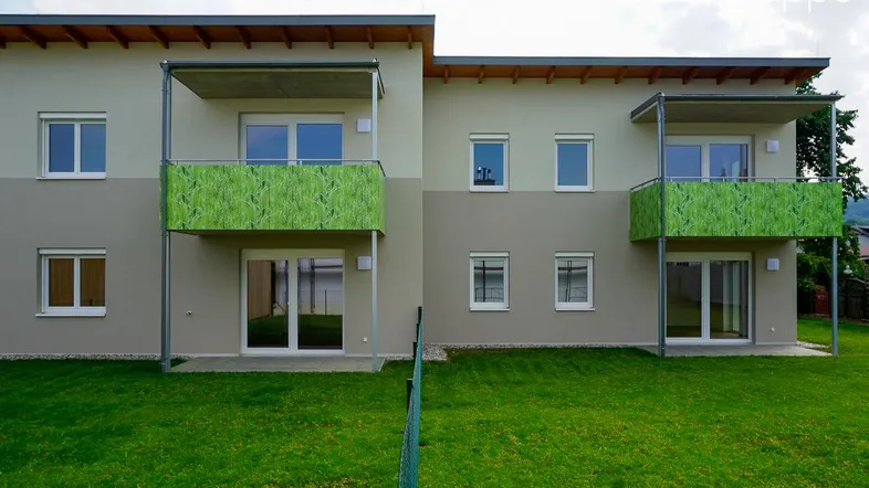 Moderne Wohnanlage mit Balkonen und gepflegter Rasenfläche, umgeben von Grün.
