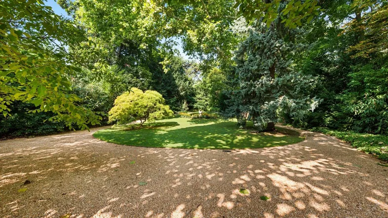 Weitläufiger Gartenbereich mit gepflegtem Rasen, altem Baumbestand und Kieswegen.