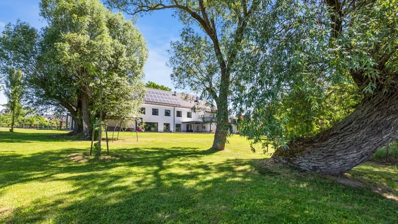Weitläufiger Garten mit großen Bäumen und Blick auf die Rückseite des Hauses mit Solaranlage.