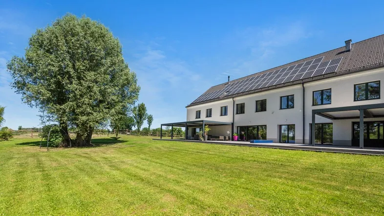 Großzügige Rasenfläche neben dem Haus mit überdachten Terrassen und Solarpaneelen auf dem Dach.