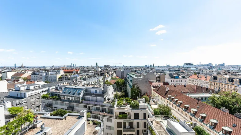 Panoramablick über die Stadt mit zahlreichen Dächern und Gebäuden unter blauem Himmel.