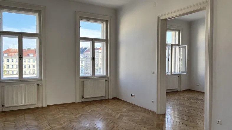 Heller Raum mit Fischgrätparkettboden und hohen Fenstern, die einen Blick auf die Stadt bieten.
