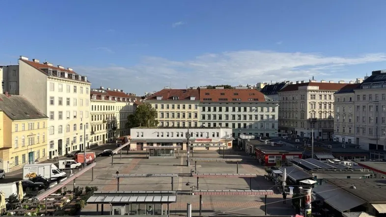 Weitläufiger Blick über einen städtischen Platz mit umliegenden Gebäuden und blauem Himmel.