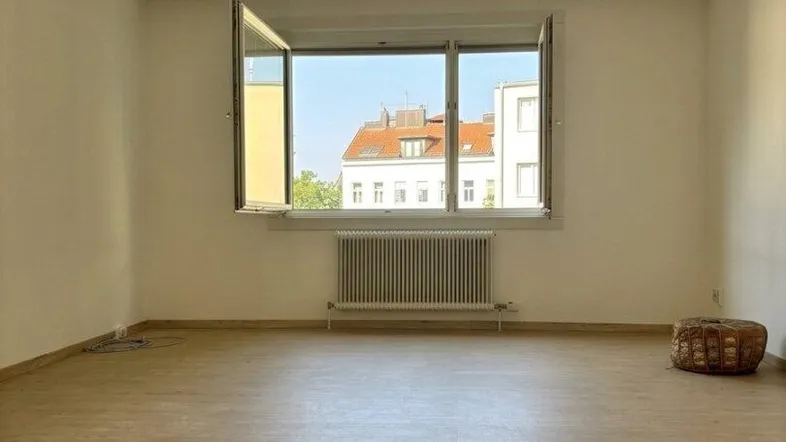 Helles, leeres Zimmer mit Laminatboden und Blick auf die umliegenden Gebäude.