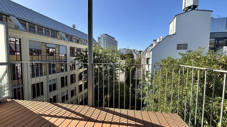 Geräumiger Balkon mit Holzboden und weitem Blick über die Stadt und umliegende Gebäude.