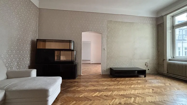 Geräumiges Wohnzimmer mit Fischgrätparkett, gemusterter Tapete und großem Fenster, das viel Tageslicht hereinlässt.