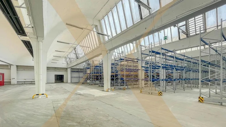 Geräumige Lagerhalle mit hohen Decken, großen Fenstern und Regalsystemen, ideal für Logistik und Lagerung.