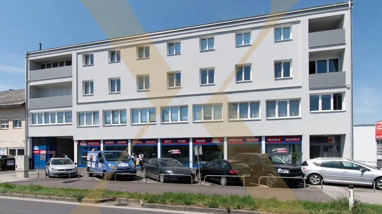 Modernes Geschäfts- und Wohngebäude mit mehreren Etagen und großen Schaufenstern im Erdgeschoss an einer Straße.