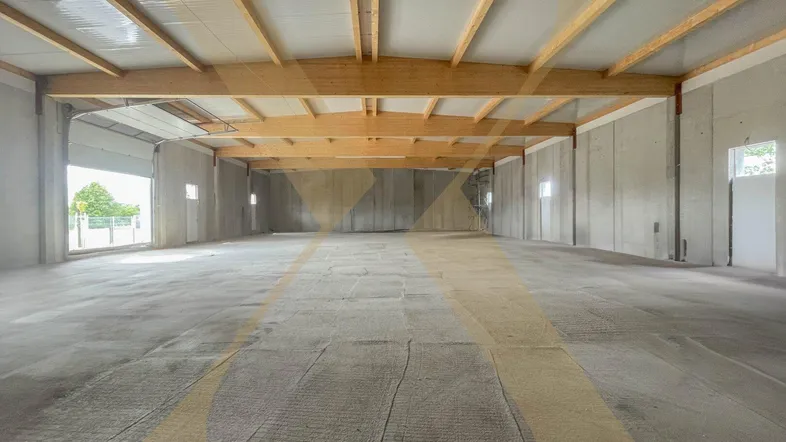 Geräumige, neuwertige Lagerhalle mit hohen Decken, sichtbaren Holzträgern und Betonboden.