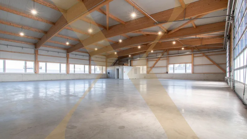 Große, helle Lagerhalle mit hohen Holzdecken und poliertem Betonboden, ideal für gewerbliche Nutzung.