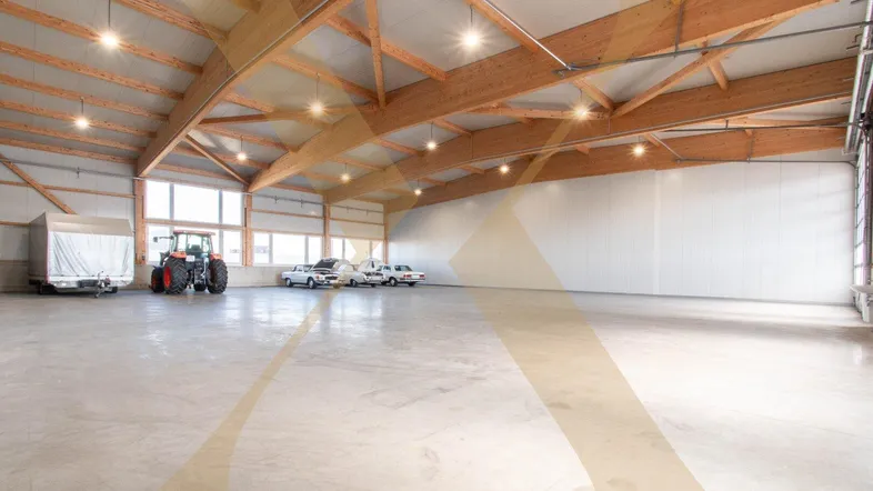 Geräumige und helle Lagerhalle mit hohen Holzdecken und robustem Betonboden, ideal für Fahrzeuge und Lagerung.