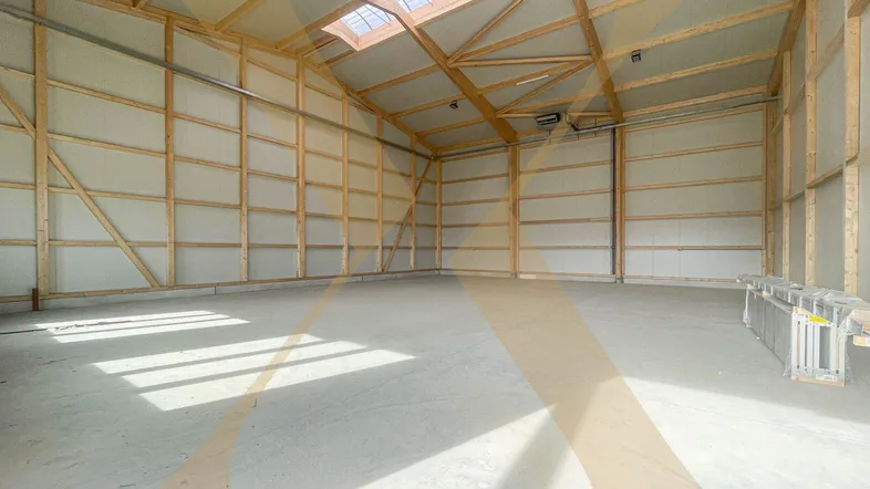 Geräumige, leere Lagerhalle mit hohen Decken, sichtbaren Holzbalken und viel Tageslicht durch Oberlichter.