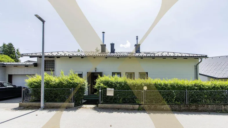 Einfamilienhaus mit gepflegtem Vorgarten und Hecke unter blauem Himmel.