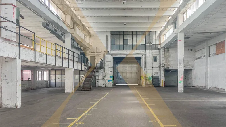 Große, leere Industriehalle mit hohen Decken, vielen Fenstern und einer Rampe zum oberen Bereich.