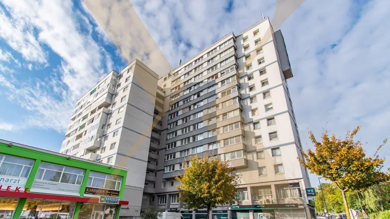Mehrstöckiges Wohngebäude mit Geschäften im Erdgeschoss unter einem bewölkten Himmel.