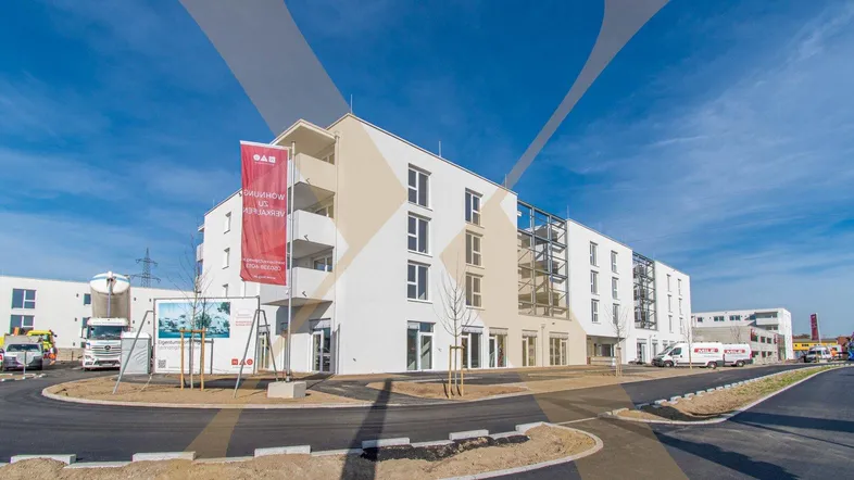 Modernes, weißes Gebäude mit Balkonen und großen Glasflächen in einer neu entwickelten Umgebung.