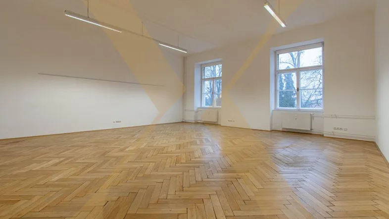 Geräumiger, heller Raum mit Fischgrätparkett, hohen Decken und großen Fenstern, die viel Tageslicht hereinlassen.