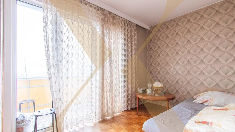 Schlafzimmer mit Parkettboden, gemusterter Tapete und Zugang zum Balkon.