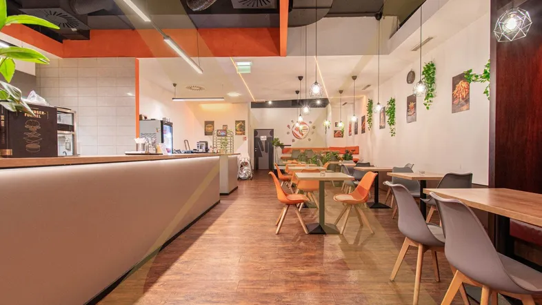 Geräumiger Restaurantbereich mit modernen Tischen und Stühlen, langer Theke und Holzboden.