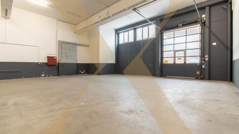 Geräumige Lagerhalle mit Betonboden, hohen Decken und einem großen Rolltor für den Zugang.
