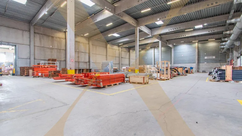 Geräumige Lagerhalle mit hoher Decke, Betonboden und Tageslicht durch Oberlichter für effiziente Nutzung.