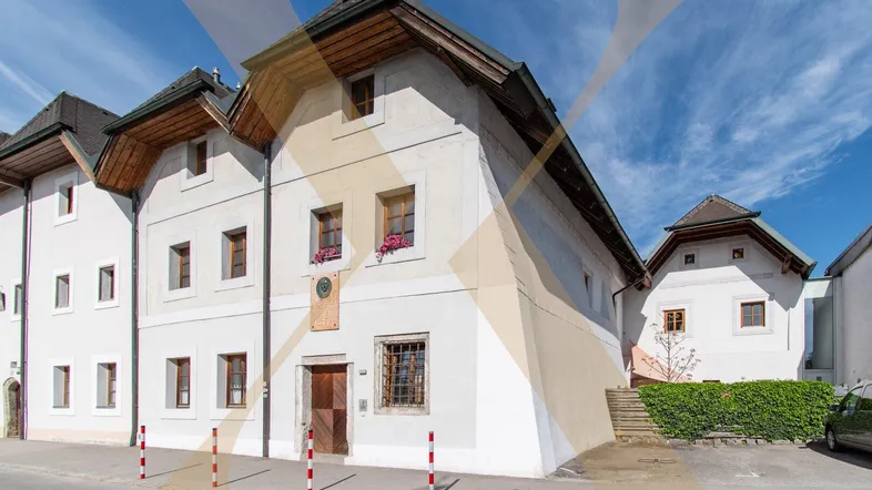 Historisches weißes Gebäude mit Holzdach und kleinen Fenstern an einer Straße.