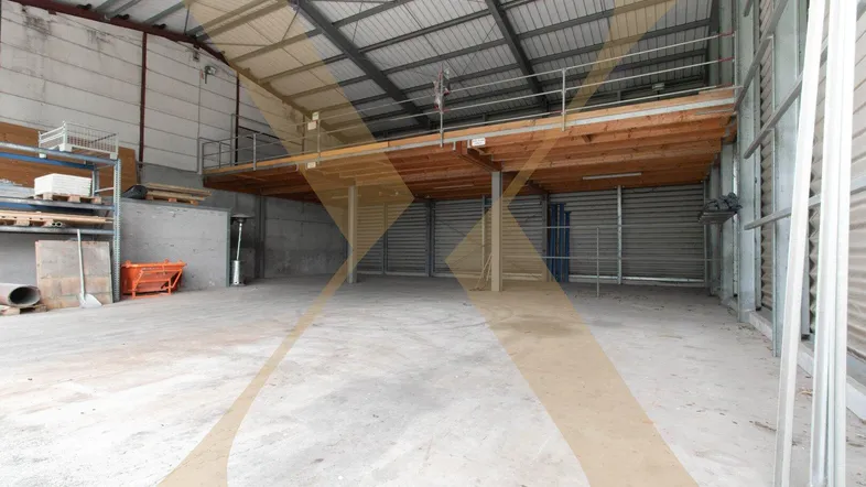Geräumige Lagerhalle mit hoher Decke, Betonboden und einer Holz-Stahl-Zwischenebene für zusätzlichen Stauraum.