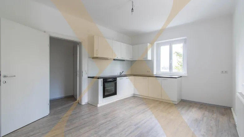 Helle Küche mit weißen Einbauschränken, integriertem Backofen und Fenster mit Blick ins Grüne.