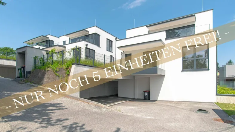 Moderne weiße Neubauten mit Flachdächern und Tiefgaragenzufahrt unter blauem Himmel.