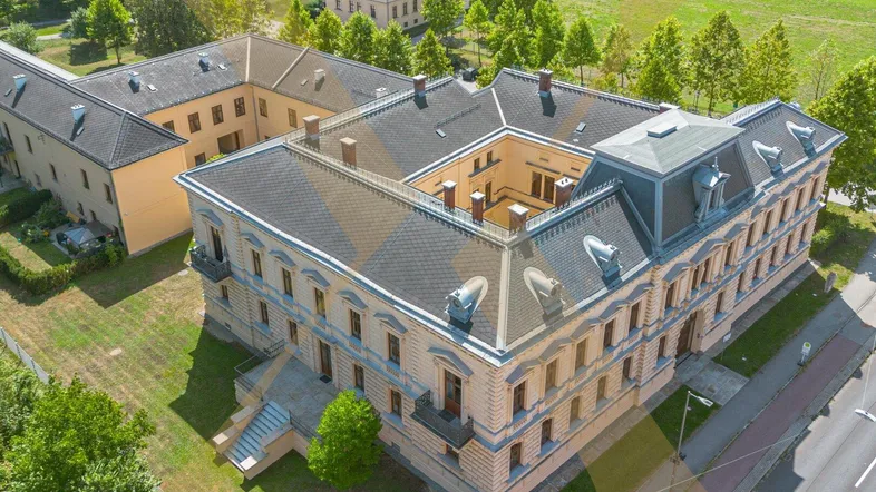 Luftaufnahme eines historischen Gebäudes mit Innenhof, umgeben von Grünflächen und Bäumen.