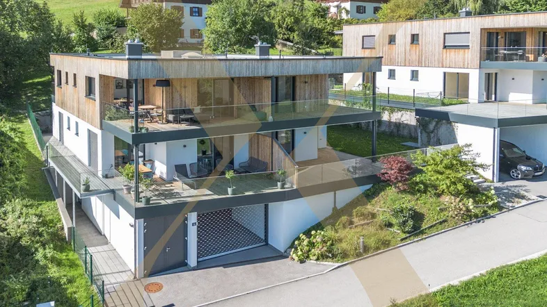 Moderne Mehrfamilienhäuser mit Holzfassade, Glasbalkonen und integrierten Garagen in grüner Umgebung.