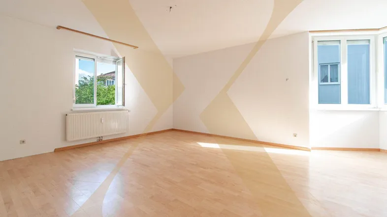 Helles Zimmer mit Parkettboden und großen Fenstern, die viel Tageslicht hereinlassen.