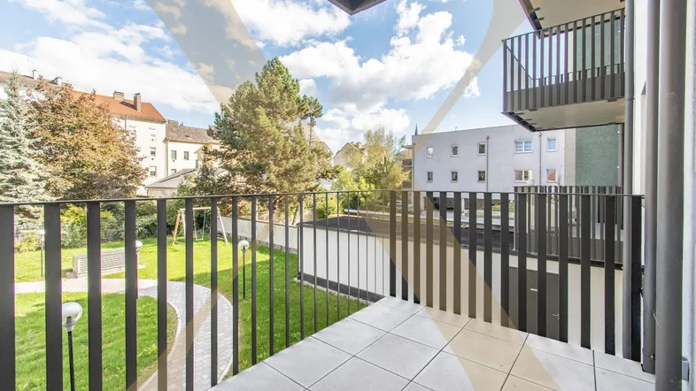 Moderner Balkon mit Fliesenboden und Blick auf den grünen Innenhof und Spielplatz.