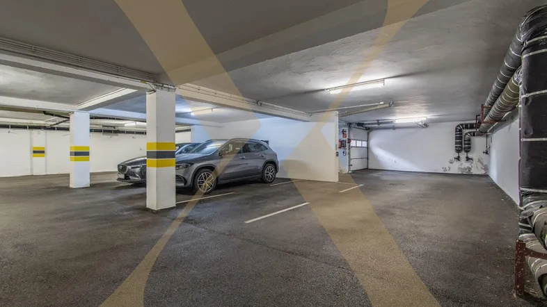 Geräumige Tiefgarage mit mehreren Stellplätzen, Betonpfeilern und sichtbaren Versorgungsleitungen.