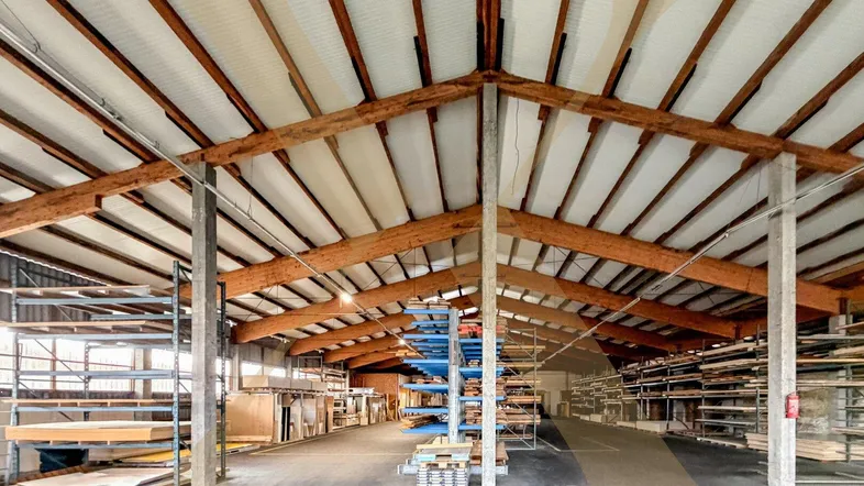 Geräumige Lagerhalle mit hoher Decke, sichtbaren Holzträgern und Regalsystemen für Materialien.