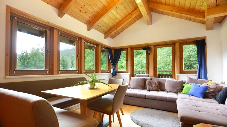 Helles Wohn- und Esszimmer mit Holzbalkendecke, großen Fenstern und Bergblick.