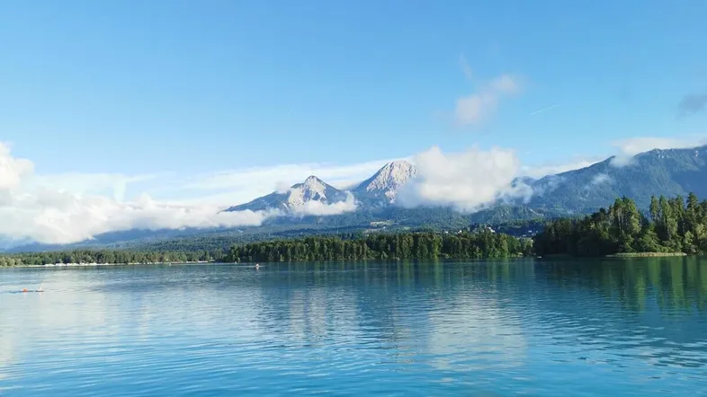 Atemberaubender Blick auf einen klaren See mit majestätischen Bergen und üppigen Wäldern im Hintergrund.