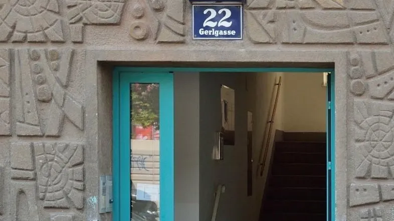 Eingangsbereich eines Gebäudes mit dekorativer Fassade, offener Tür und Treppenhaus im Inneren.