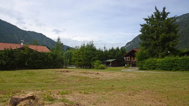 Weitläufige Grünfläche mit Blick auf traditionelle Häuser und die umliegende Berglandschaft.