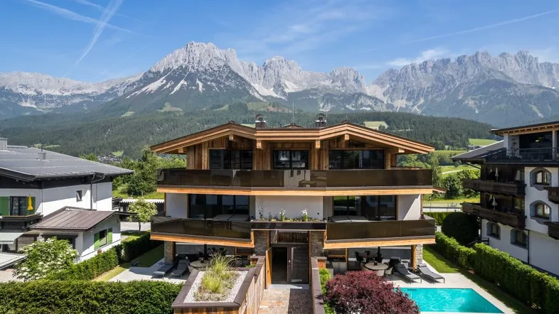 Modernes Chalet mit Holzelementen, Pool und atemberaubendem Bergblick unter blauem Himmel.