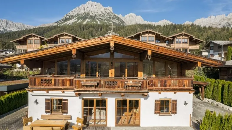 Traditionelles Holzhaus im Alpenstil mit Bergblick und Balkonen unter blauem Himmel.