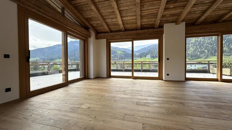 Geräumiger Wohnbereich mit Holzbalkendecke, Holzboden und großen Fenstern mit Bergblick.