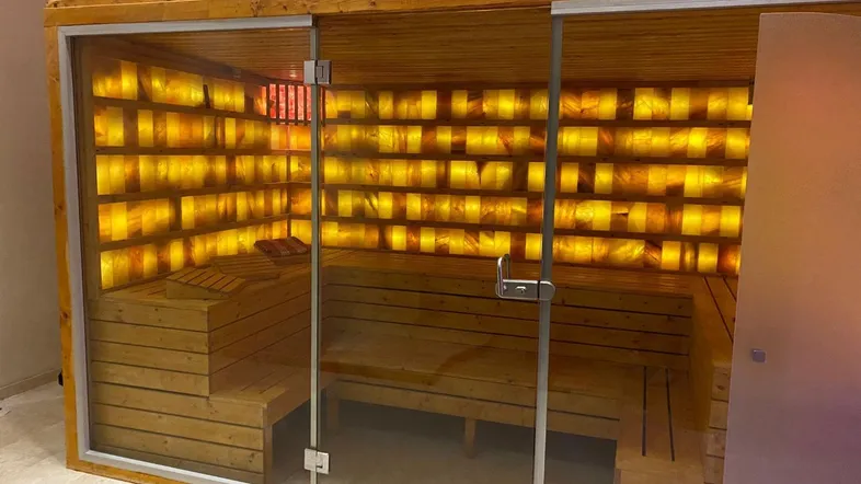 Moderne Sauna mit Holzbänken, Glasfront und beleuchteter Salzwand für entspannende Momente.