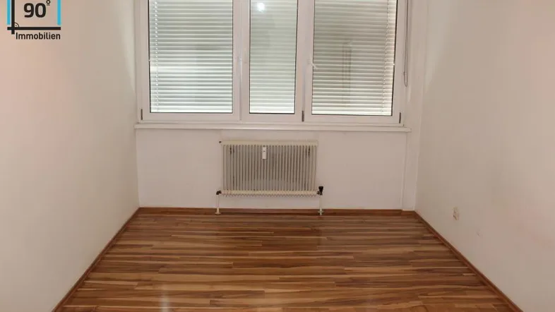 Heller Raum mit Holzfußboden, großem Fenster und Heizkörper.