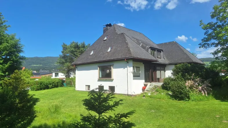 Freistehendes Haus mit großem Garten und Blick auf die umliegende Berglandschaft unter blauem Himmel.