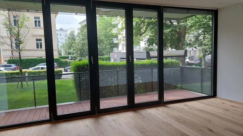 Helles Wohnzimmer mit großen Fenstern, Holzboden und Zugang zu einem Balkon mit Blick ins Grüne.
