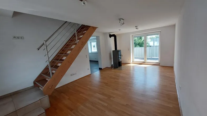 Helles Wohnzimmer mit Holzboden, Kaminofen und Zugang zu einem Balkon oder einer Terrasse.
