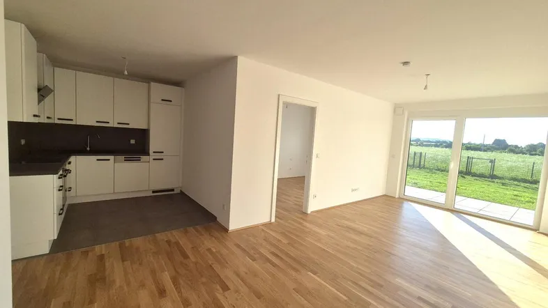 Helles, offenes Wohnzimmer mit integrierter Küche, Parkettboden und Zugang zur Terrasse mit Weitblick.