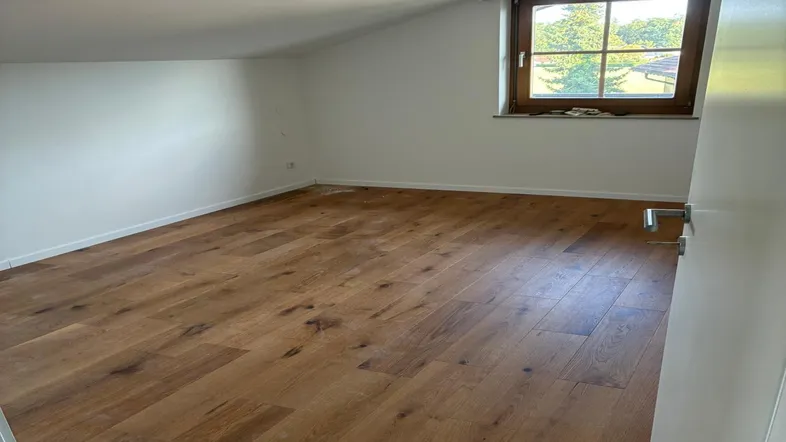 Helles Zimmer im Dachgeschoss mit Holzboden und schrägen Wänden, ideal als Schlaf- oder Arbeitszimmer.