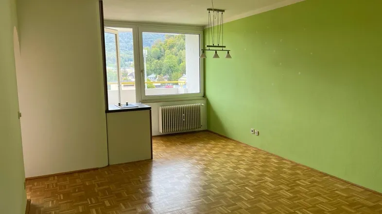 Helles Wohnzimmer mit Parkettboden, grüner Wand und Blick auf die umliegende Landschaft.